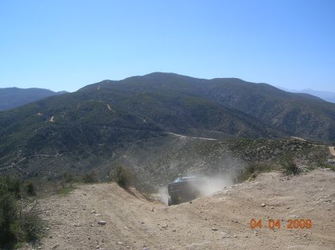 1985 Ford Bronco - Off-road vehicle navigating a dusty, steep trail in a mountainous area.