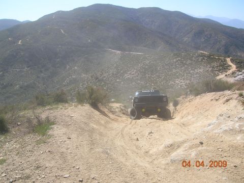 1985 Ford Bronco - A black off-road truck navigates a dusty trail in a mountainous, arid landscape.