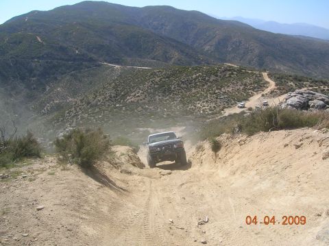 1985 Ford Bronco - A white Ford Bronco navigates a steep, dusty off-road trail in a mountainous landscape.