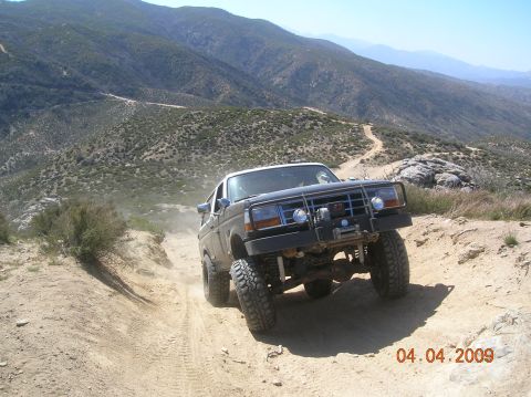 1985 Ford Bronco - Ford Bronco navigates a steep, dusty trail in a mountainous, arid landscape.