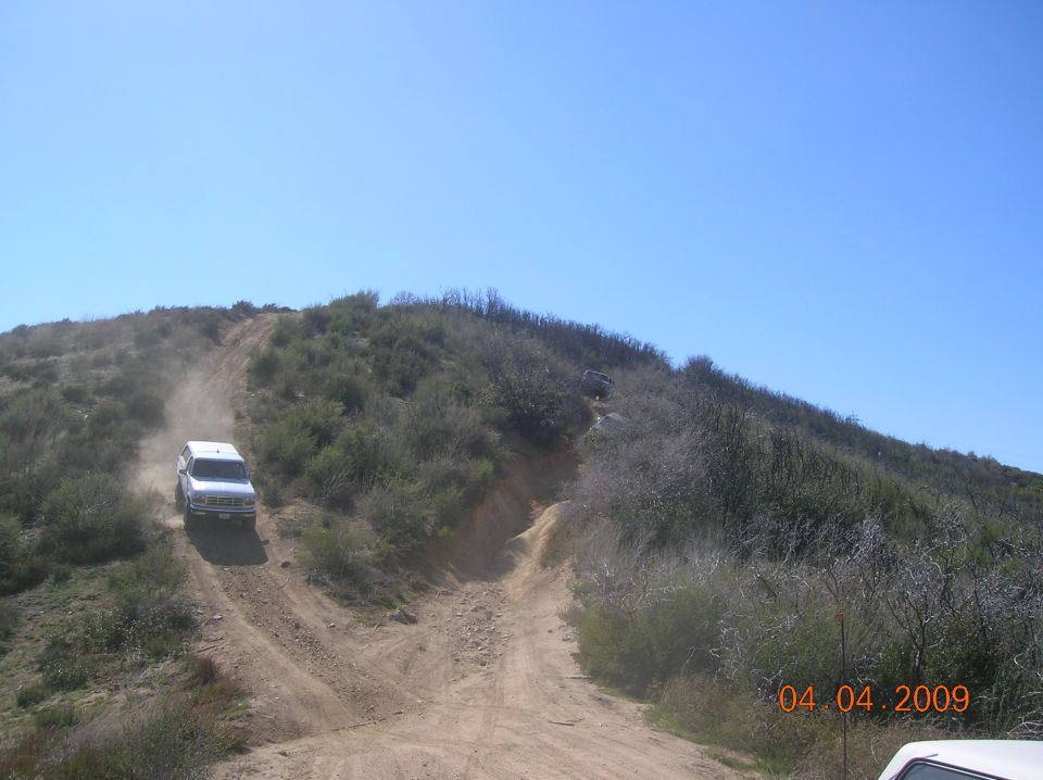 White SUV driving up a dusty dirt hill, another vehicle further up the trail