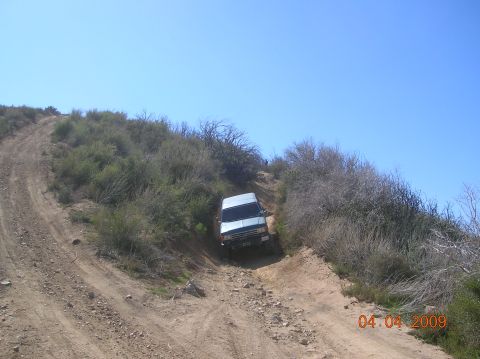 1985 Ford Bronco - A white SUV navigates a challenging off-road trail on a clear day.
