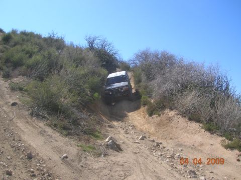 1985 Ford Bronco - A white SUV navigates a challenging off-road trail on a sunny day.