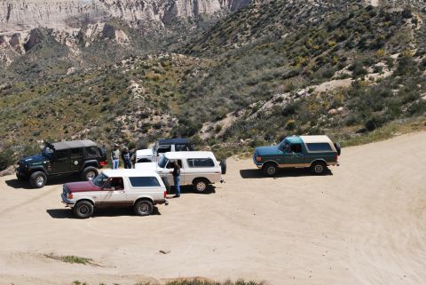 1996 Ford Bronco - Several SUVs and trucks, including a 1996 Ford Bronco, are gathered on a dusty mountain road.
