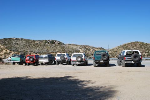 1996 Ford Bronco - A group of Ford Bronco SUVs are parked in a desert landscape under a clear blue sky.
