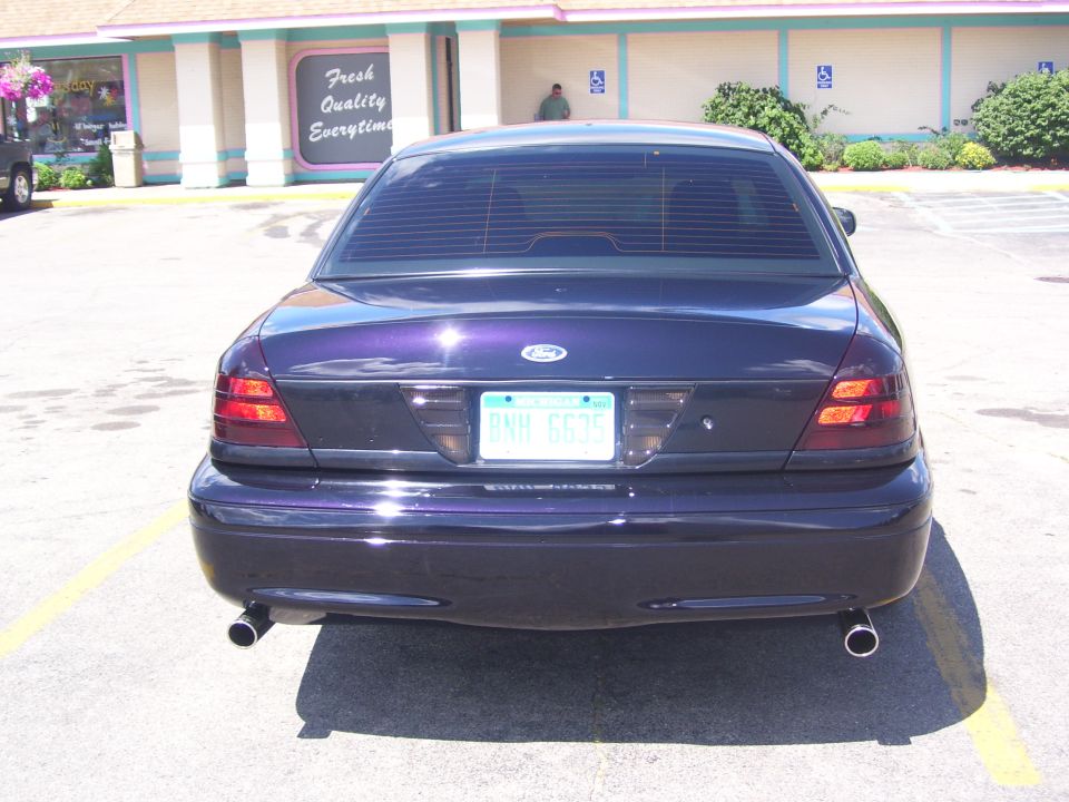Rear view of a dark Ford full-size sedan with dual exhaust in a lot