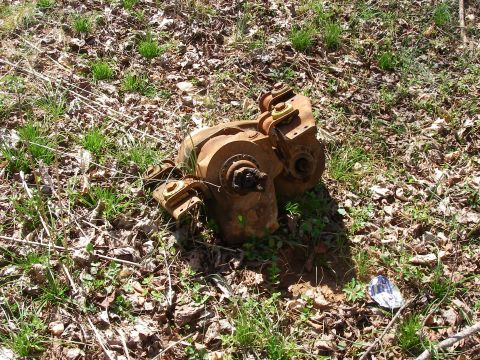 1978 Ford Bronco - A heavily rusted mechanical component lies discarded on the ground amidst grass and fallen leaves.