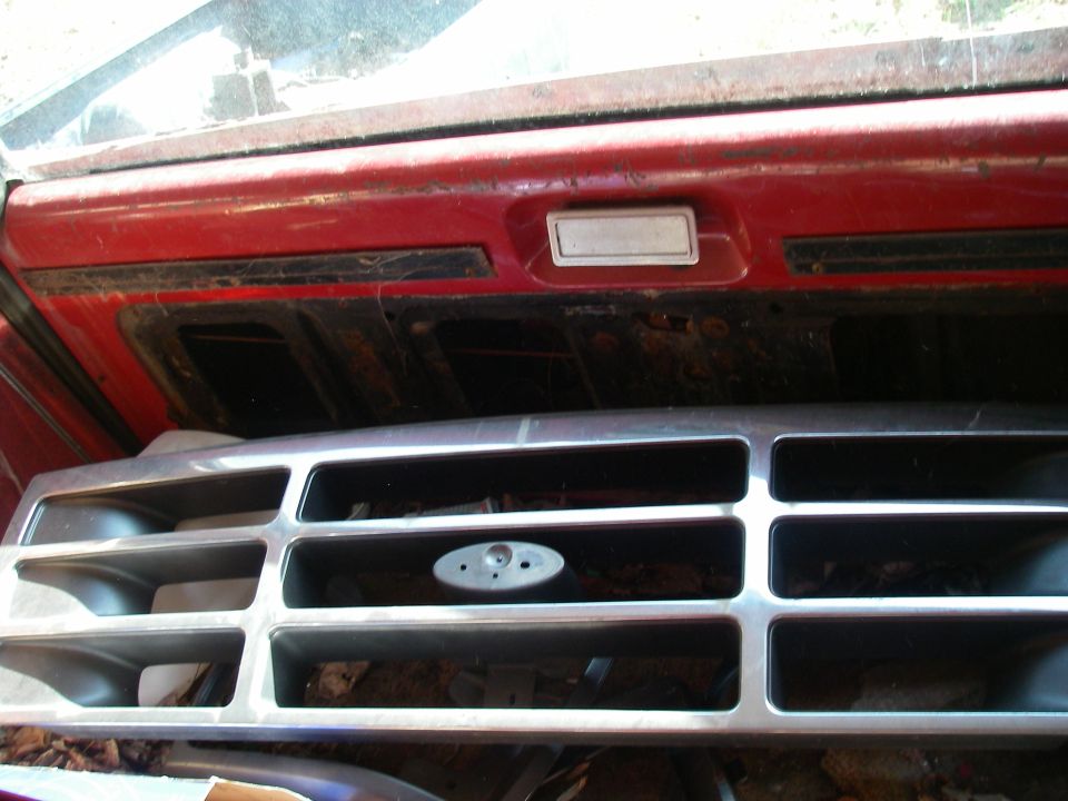 Close-up of a vehicle's front grille and part of the dashboard. The grille has horizontal bars and an oval emblem mount