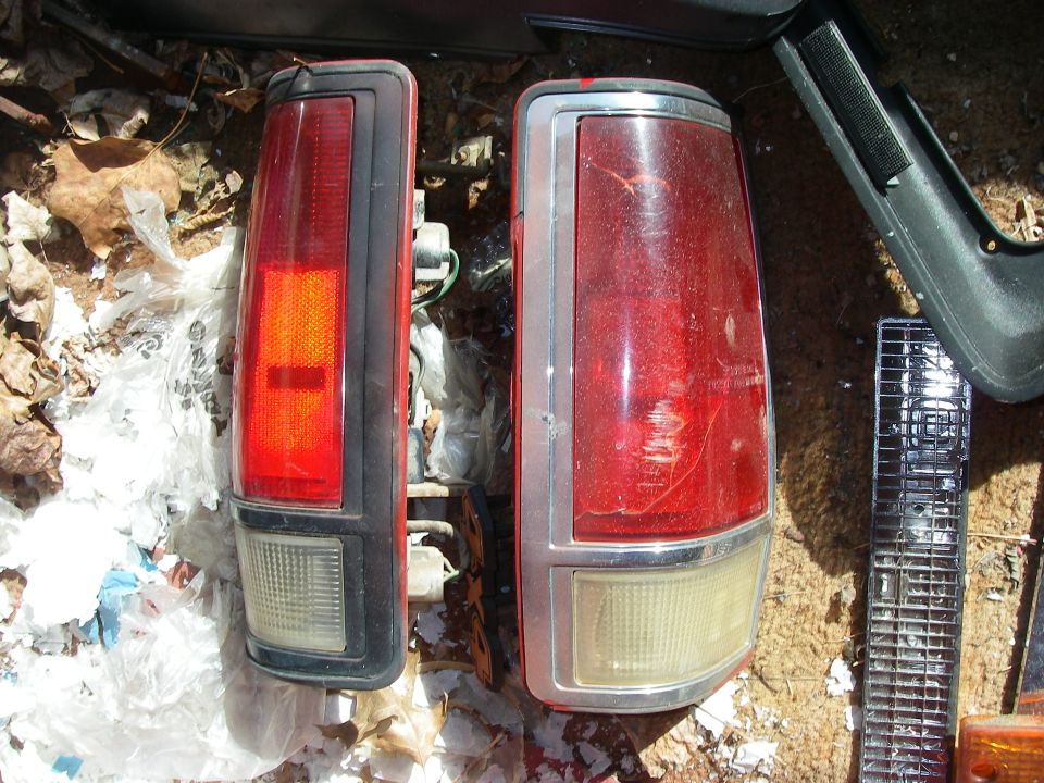 Two red tail lights, one with a black bezel and one with a chrome bezel, lie on the ground