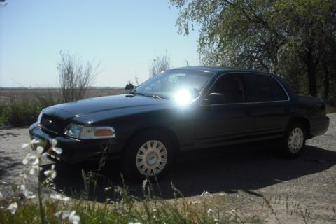 2003 Ford Crown Victoria - A dark 2003 Ford Crown Victoria sedan is parked outdoors under a clear sky.