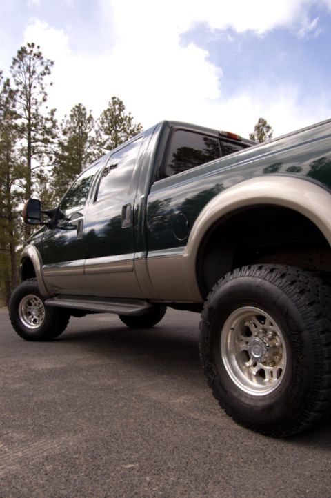2003 Ford F-350 - This dark green and tan pickup truck is shown from a 3/4 front angle, highlighting its build and off-road tires.