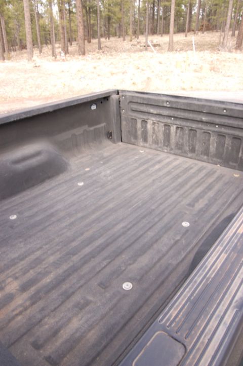 2003 Ford F-350 - The interior of a truck bed is shown from a high angle, with a wooded area in the background.