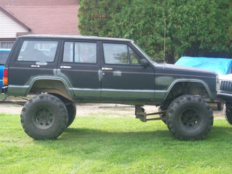 1900 Acura CL - A modified Jeep Cherokee XJ with large off-road tires sits on grassy terrain next to another vehicle.