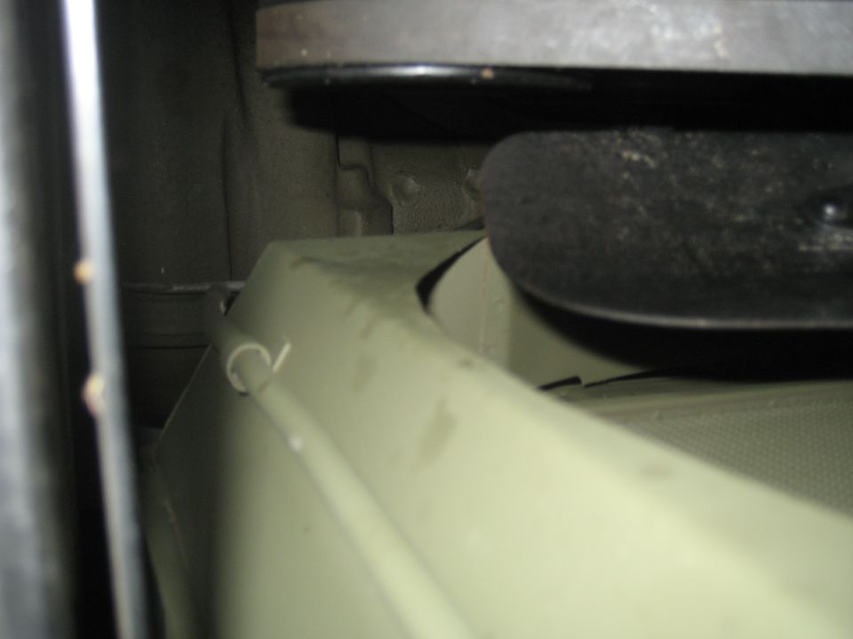 Underside of a vehicle showing a light green panel with a wire clip and a dark circular object above.