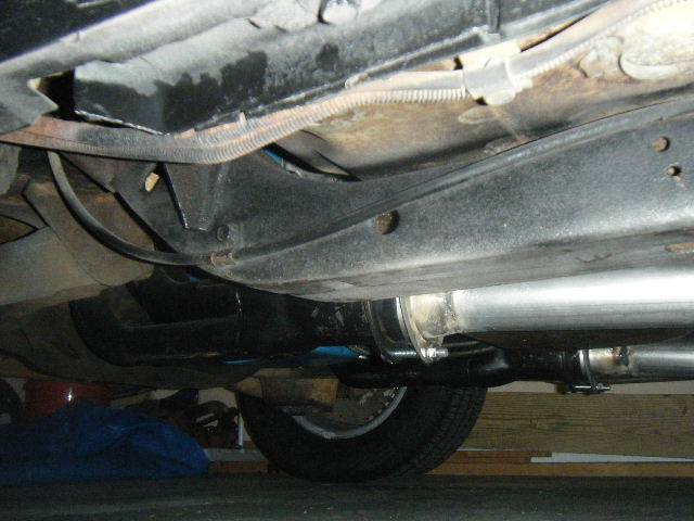 Underside of a vehicle frame and exhaust system with muffler and pipes.
