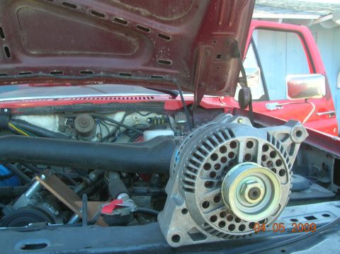 1985 Ford Bronco - The open hood of a red vehicle reveals its engine bay, with a large alternator prominently displayed in the foreground. The vehicle appears…