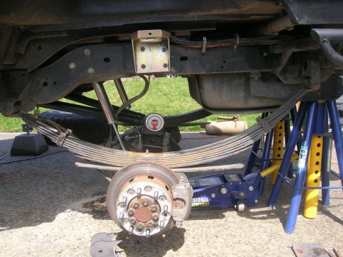 1996 Ford Bronco - The undercarriage of a vehicle is shown, with the rear suspension, leaf springs, shock absorber, brake rotor, and a portion of the tire vis…