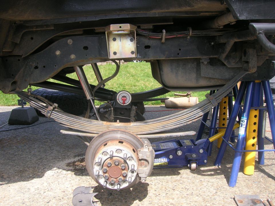 Undercarriage of a vehicle showing suspension components, jack stands, and a jack.