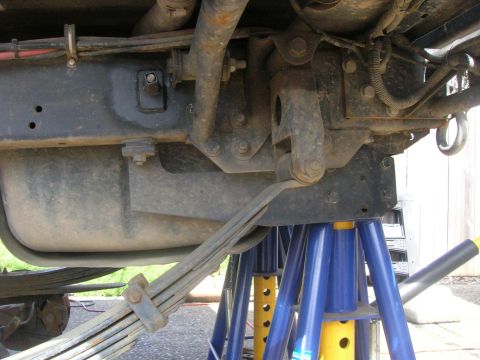 1996 Ford Bronco - The undercarriage of a vehicle is shown, supported by blue and yellow jack stands. A leaf spring suspension system and a fuel tank are visi…