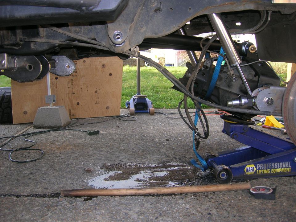 Underside of a vehicle with suspension components and a hydraulic jack.