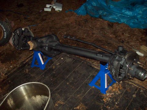 1989 Ford F-150 - A black Ford F-150 front axle assembly is supported by two blue jack stands on a wooden surface. A tire with visible text is to the left of…