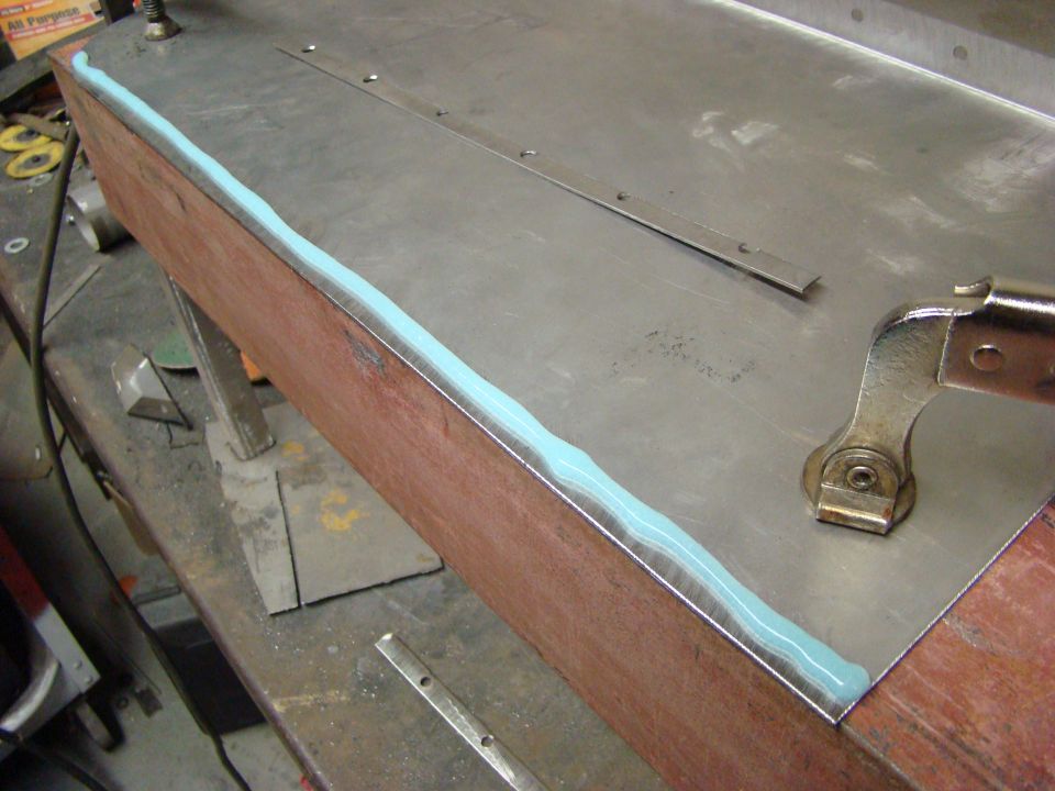 Close-up of sealant on a metal and wood surface with a clamp.