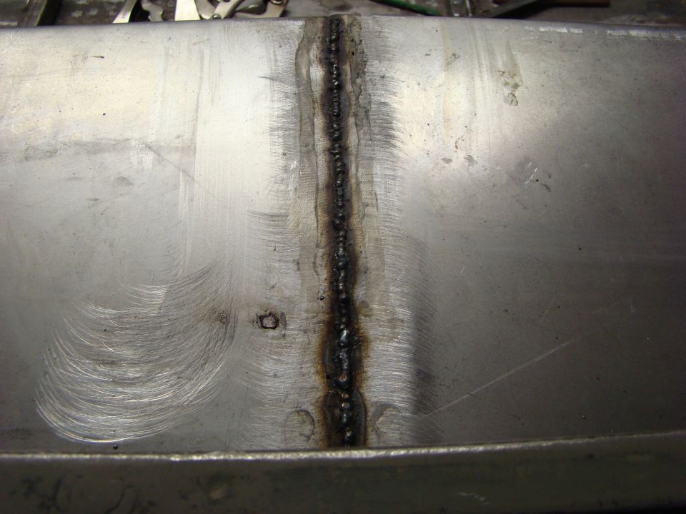 Metal panel with a vertical weld seam, showing circular grinding marks and some dark discoloration