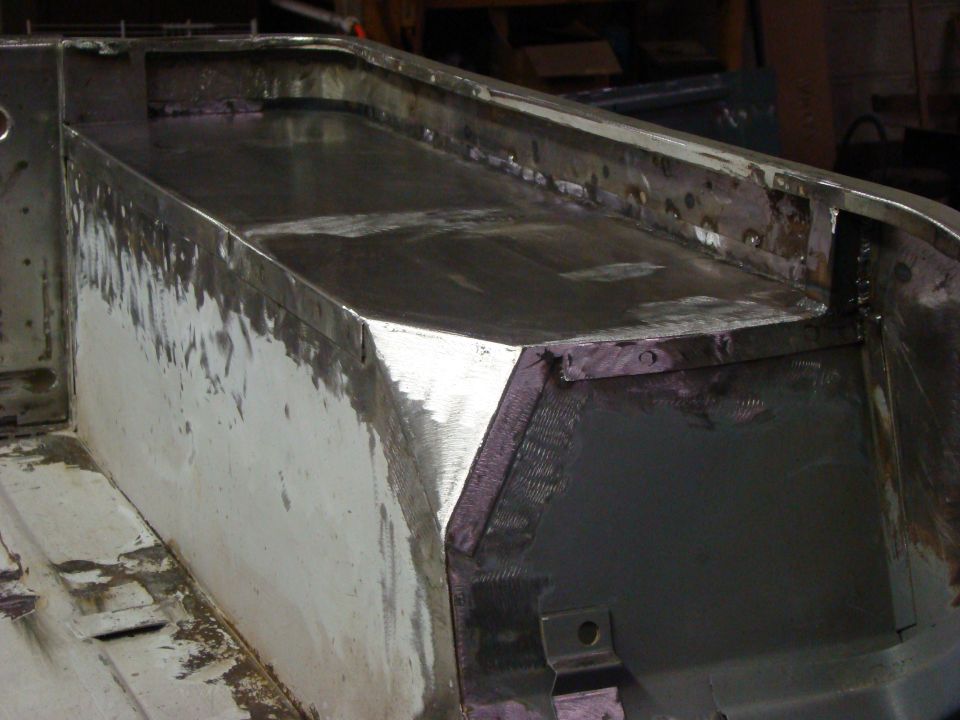 Close-up of metal fabrication work on the interior of a vehicle bed, showing freshly welded seams and a painted surface