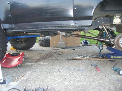 1996 Ford Bronco - The underside of a black SUV is shown with its rear axle supported by a blue hydraulic jack. A large metal rod extends from the frame to th…