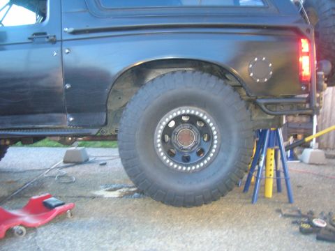 1996 Ford Bronco - The rear passenger side of a black Ford Bronco is shown lifted on jack stands. The vehicle features large off-road tires and a custom rear…