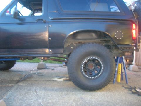 1996 Ford Bronco - The rear passenger side of a dark-colored Ford Bronco is shown, lifted on jack stands. The vehicle features large off-road tires and visibl…