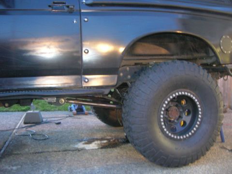 1996 Ford Bronco - The side view of a dark-colored Ford Bronco shows its large off-road tire and suspension components. A blue hydraulic jack is visible under…
