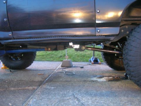 1996 Ford Bronco - The underside of a dark-colored SUV is shown, with the rear tire and suspension components visible. The vehicle is supported by a blue jack…