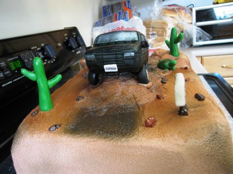 1986 Ford Bronco - Novelty desert-diorama cake on a kitchen stove, topped with a hand-sculpted black fondant Bronco-style SUV wearing a "ZUNBAJA" license plat…