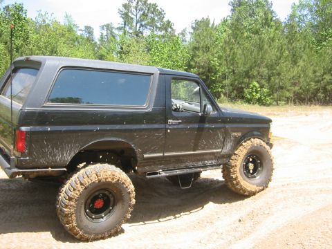 1995 Ford Bronco - This lifted black Ford Bronco is covered in mud, indicating off-road use.