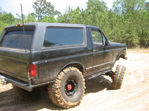 1995 Ford Bronco - Modified black Ford Bronco with off-road tires and suspension sits on a dirt track.