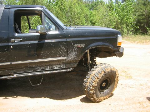 1995 Ford Bronco - This lifted Ford Bronco is covered in mud, indicating it has been off-roading. The vehicle is parked on a dirt surface with trees in the ba…