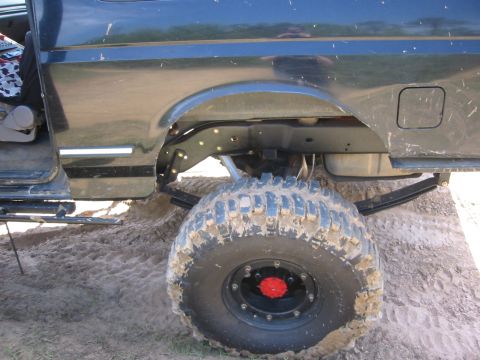 1995 Ford Bronco - The rear driver's side tire and suspension of a dark colored Ford Bronco is shown in this close-up, low-angle shot. The vehicle is parked i…