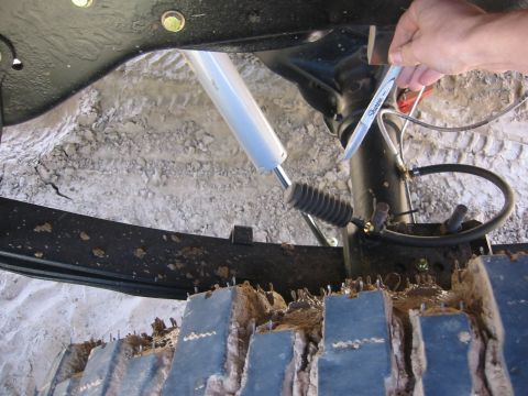 1995 Ford Bronco - A close-up view of the underside of a vehicle, showing suspension components, a shock absorber, and part of a track system covered in mud.