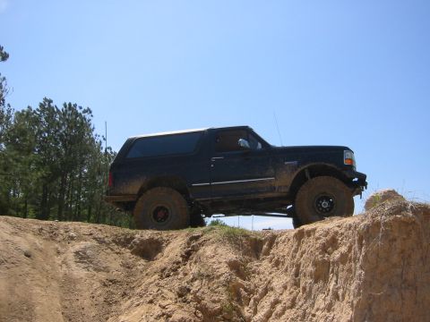 1995 Ford Bronco - A black Ford Bronco is parked on the edge of a dirt embankment under a clear blue sky. The vehicle is angled to the right, showing its side…