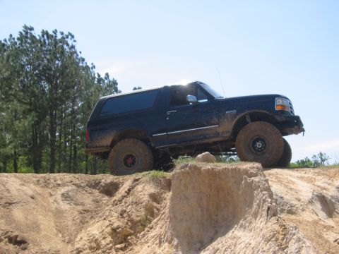 1995 Ford Bronco - A dark blue Ford Bronco is parked on a dirt hill with large off-road tires. The vehicle is angled upwards, showing its side profile against…