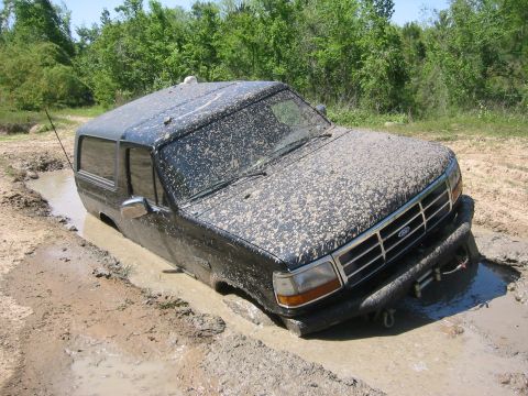 1995 Ford Bronco - A black 1995 Ford Bronco is stuck deep in a muddy mire, its tires submerged.