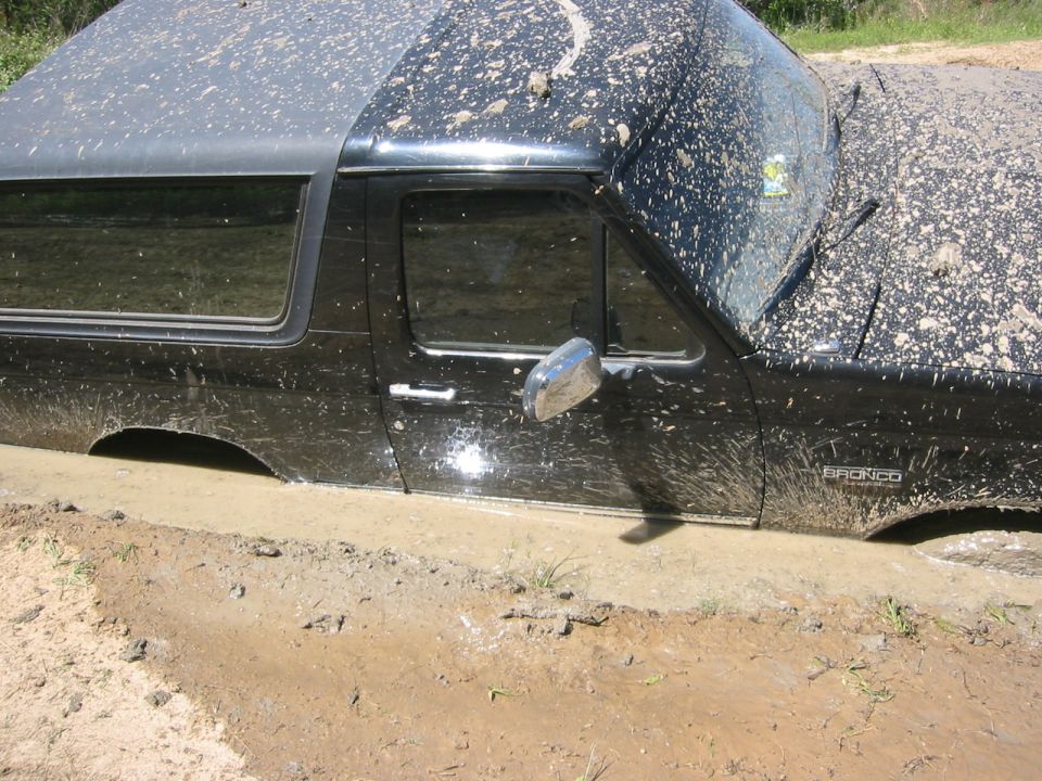 Black 1995 Ford Bronco stuck in mud, side view. Mud splattered all over the vehicle