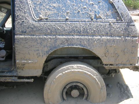 1995 Ford Bronco - This 1995 Ford Bronco is heavily covered in mud, with the driver's door ajar and the rear wheel submerged.