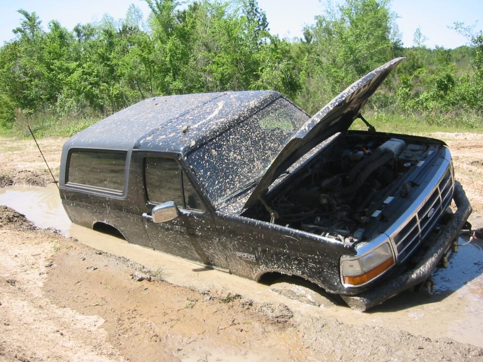 1995 Ford Bronco stuck in mud, hood open, covered in mud