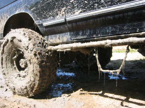 1995 Ford Bronco - A heavily mud-caked vehicle is stuck in the mire, with water dripping from its undercarriage.