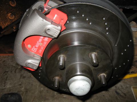 1968 Shelby GT500 - Close-up of a car's front brake assembly, showing a caliper, red brake pads, and a drilled rotor.