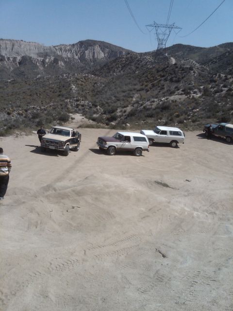 1982 Ford Bronco - Several vehicles, including a brown and white Ford Bronco, are parked in a dusty, mountainous area.
