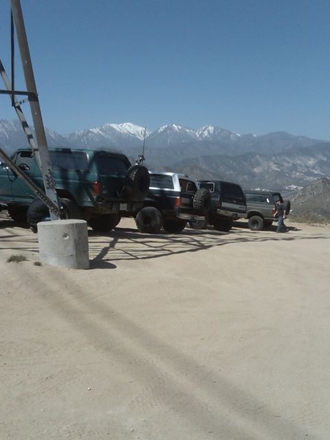 1982 Ford Bronco - A line of SUVs parked on a dusty lot, with a mountain range visible behind them.