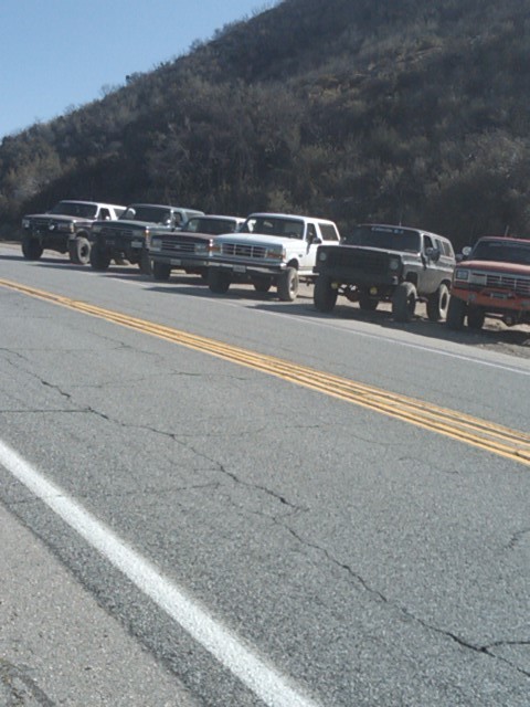 1982 Ford Bronco - Several Ford Broncos are parked in a line along a rural road.